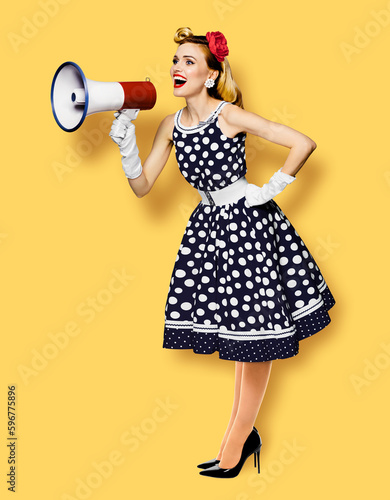 Full body length image of beautiful woman hold mega phone, shout advertise. Pretty girl in black pin up dress, with megaphone loudspeaker. Isolated on orange yellow background. Big sales ad.