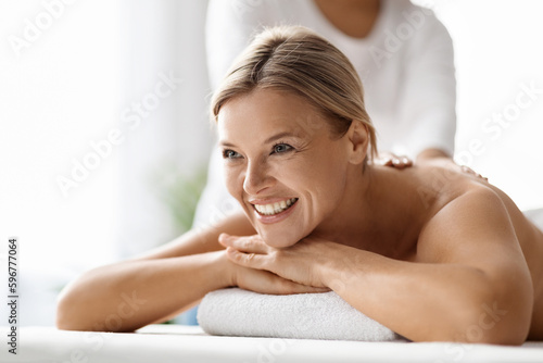 Closeup of beautiful middle aged woman enjoying back massage at spa salon