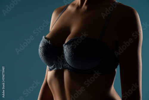 Close up on woman torso in the shadow. Blue bra and natural breasts cleavage on a blue background