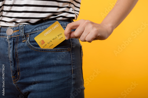 hand of person woman holding plastic credit card out of the pocket blue jean plants isolated on yellow studio background. online shopping payment, bill, currency, pay money, finance concept.