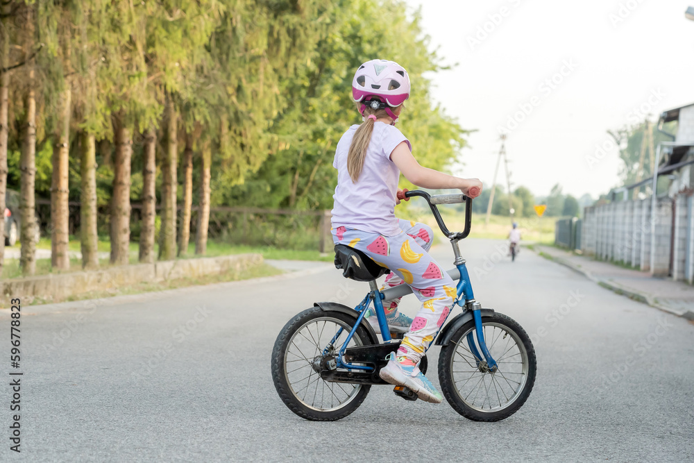 Anonymous school age girl riding an old used retro second hand repurposed bike on an empty country road, summer vacations, rural area, back. Copy space, one person, kids cycling, biking, activities Anonymous school age girl riding an old used retro second hand repurposed bike on an empty country road, summer vacations, rural area, back. Copy space, one person, kids cycling, biking, activities