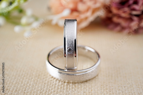 Couple white gold wedding rings on a burlap cloth with brown flowers and cream on the back