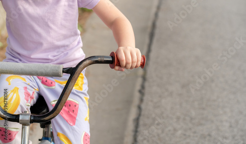 Young anonymous unrecognizable school age child riding an old used second hand bike, holding hands on handlebars closeup, detail, one person, blurred background, copy space. Old bicycle, cycling