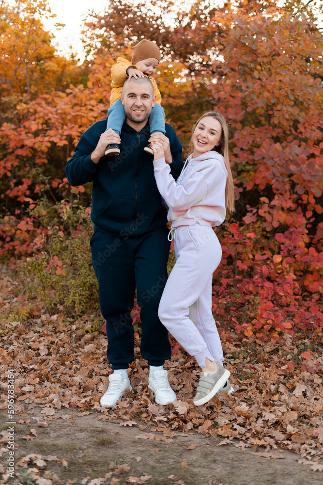 Fototapeta premium Autumn portrait of a happy family with a small child on a walk in the autumn park, sports mom, dad and son outdoors. family, childhood, season and people