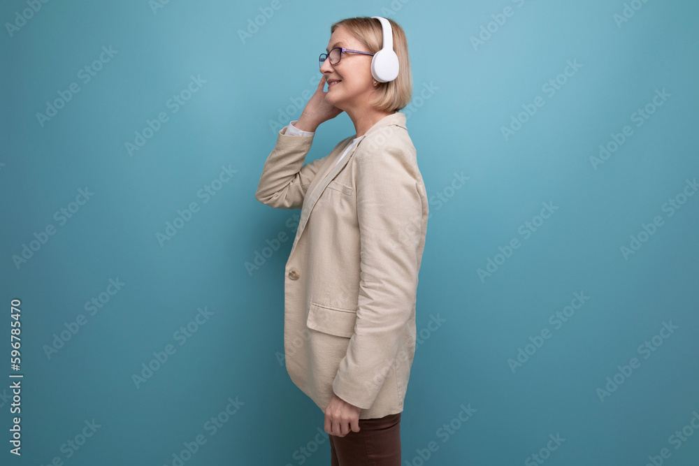 50s a woman in a jacket masters the technique for listening to music in headphones on a studio background
