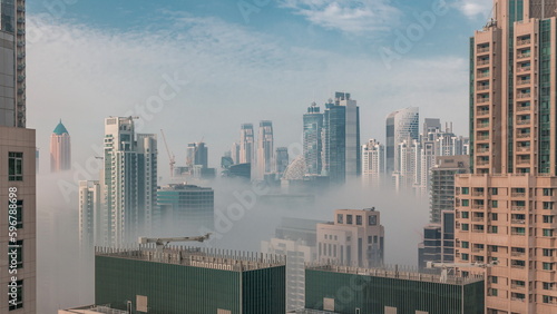 Dubai skyscrapers covered by morning fog in business bay district during sunrise timelapse.