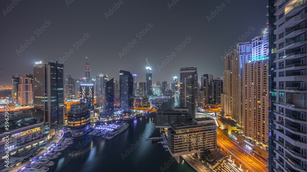 Aerial view to Dubai marina skyscrapers around canal with floating boats all night timelapse