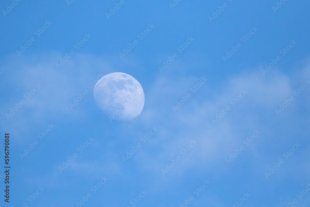 Moon in blue sky during daytime with some light clouds
