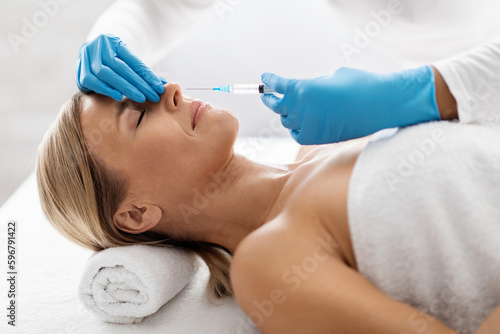 Middle aged woman receiving beauty injections for nose zone at spa salon