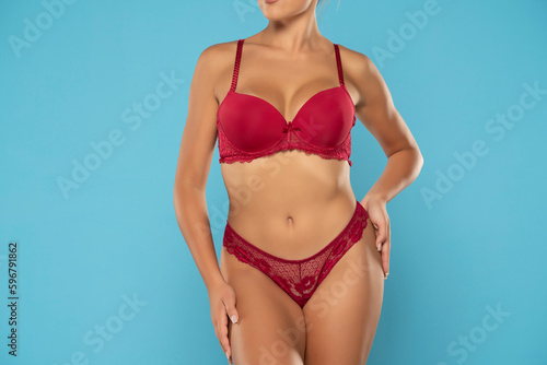 Tanned woman in top form, perfect body shape. Parts of woman body in red underwear, front view, blue background