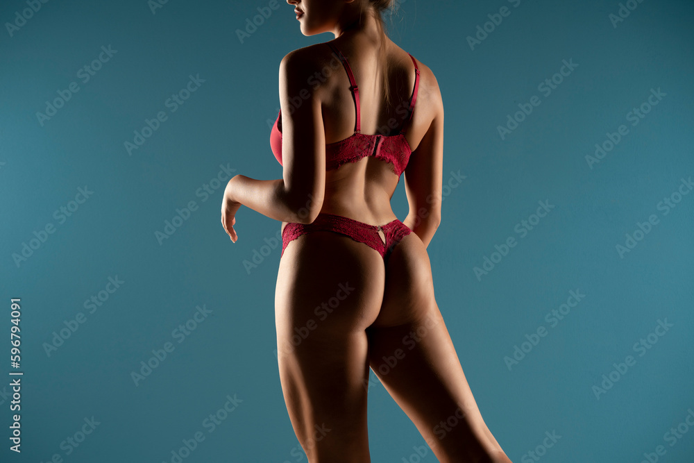 Tanned woman in top form, perfect body shape in the shadow. Parts of woman body in red underwear, back rear view, blue background