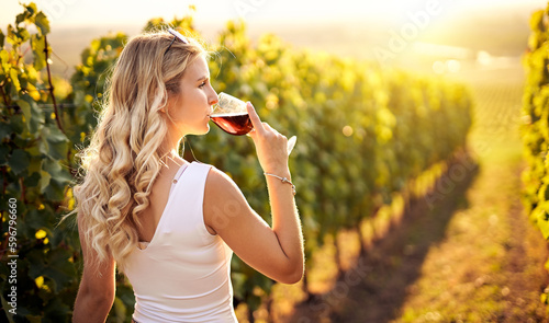 Young caucasian woman holding a glass of red wine in vineyard on sunny day, back view - Vinification, vine-growing and wine-tasting concept with a millennial young adult girl