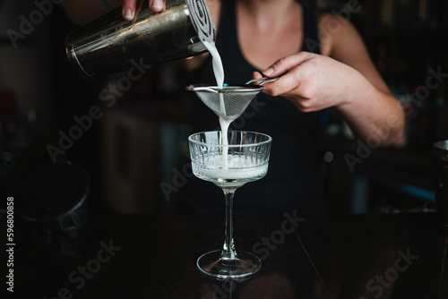 Shot of a woman bartender straining a cocktail from the shaker into the glass