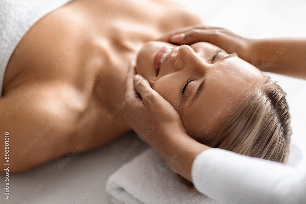 Beautiful middle aged woman enjoying face lifting massage in spa salon Beautiful middle aged woman enjoying face lifting massage in spa salon