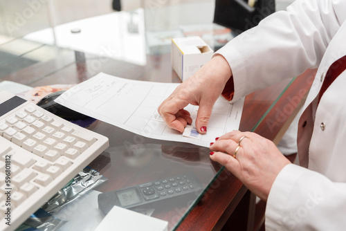 Crop woman in coat sticking barcode on paper working in pharmacy photo