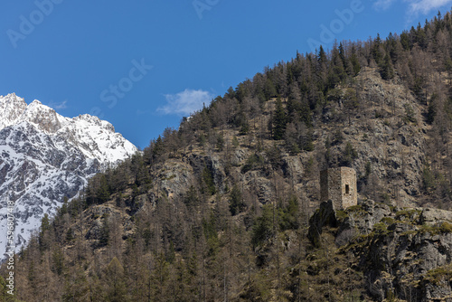 Vue sur les montagnes dans les Alpes en Italie. Colline couverte de sapins au premier plan avec une tour en ruine et montagnes enneigées à l’arrière plan 