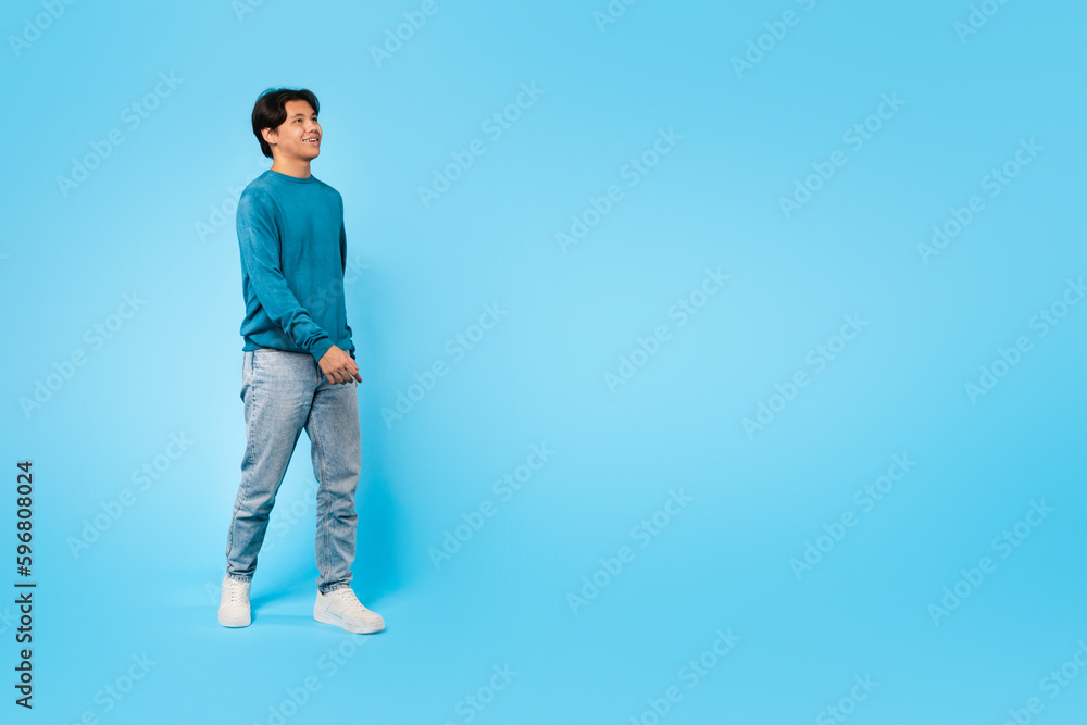 Cheerful Asian Teenager Guy Walking Looking Aside Over Blue Background Cheerful Asian Teenager Guy Walking Looking Aside Over Blue Background