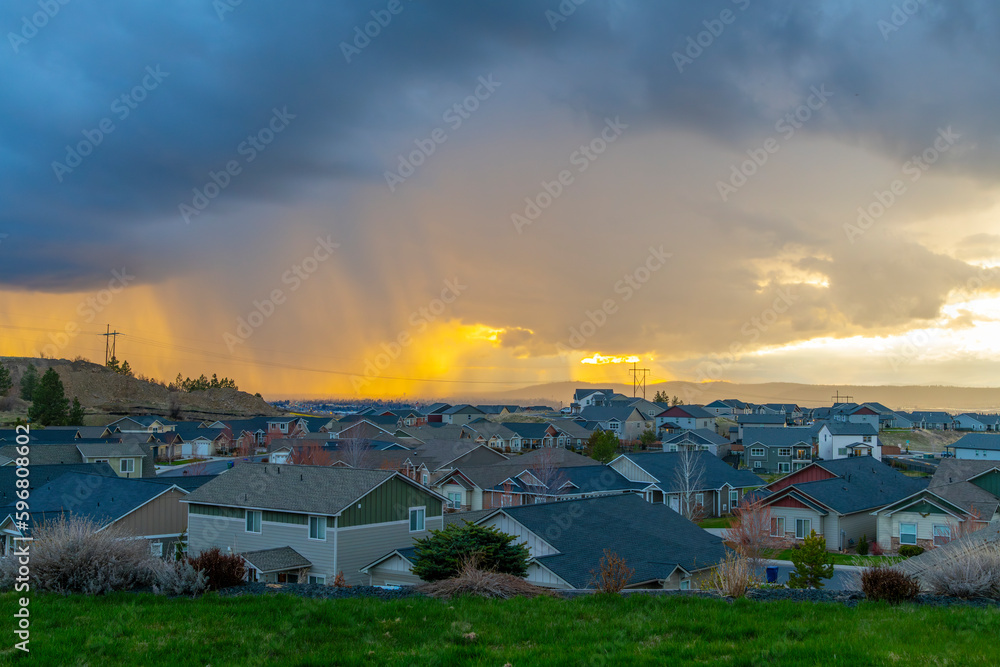 The sun breaks through heavy clouds at sunset and illuminates rain over the city of Spokane, Washington, USA, seen from a hill in the Spokane Valley area.