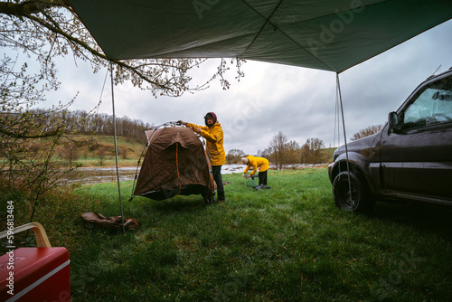 Man and woman on vacation in wilderness. preparing the camp, setting up quick folding tent system and tourist equipment. bad weather. A gloomy spring day. Camping by car.