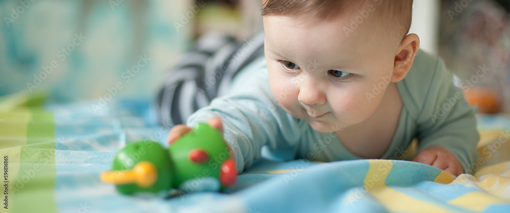 Obraz premium Portrait of cute baby boy playing with colorful toys at home while lies on its stomach. Playground for babies