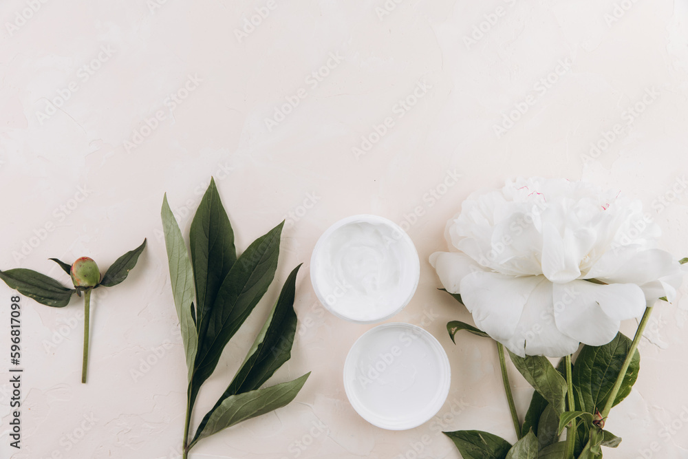 A cream mask on a light background with a delicate peony flower. Mock up image. A cream mask on a light background with a delicate peony flower. Mock up image.
