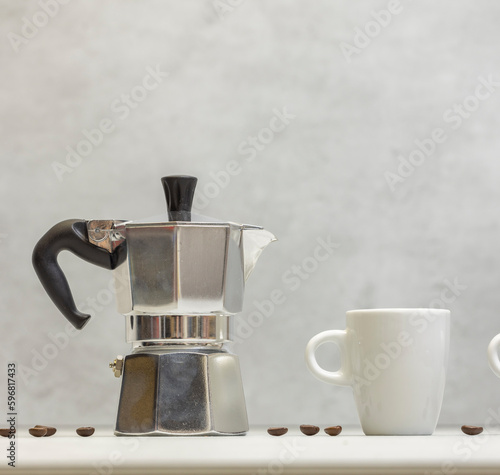 Metal geyser coffee maker on table with cup