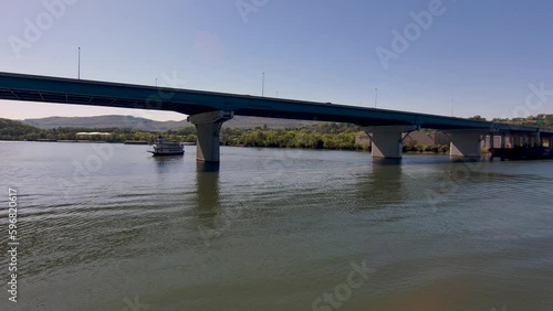 panning aerial footage of Olgiati Memorial Bridge over the rippling green waters of the Tennessee River with lush green trees, riverboats on the water and  blue sky in Chattanooga Tennessee USA photo