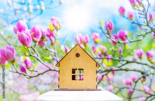 Sunlit Toy Wooden House among Blooming Magnolia Trees