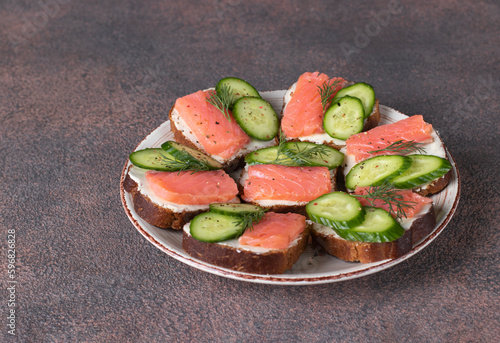 Sandwiches with salted salmon, cucumber and dill on bread on brown background. Festive snack
