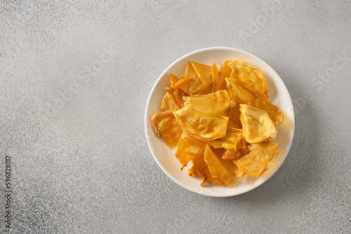 Organic dried jackfruit chips from tropical island Ceylon. Fruits chips for vegan with antioxidant, vitamin in white plate on gray background. Top view. Copy space. photo