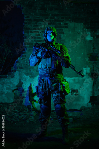 airsoft. a man in camouflage with machine guns in his hands on the ruins in the dark.