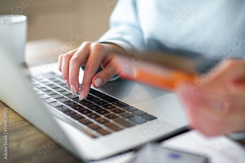 Smiling young adult woman online shopping on her laptop in the kitchen of her home