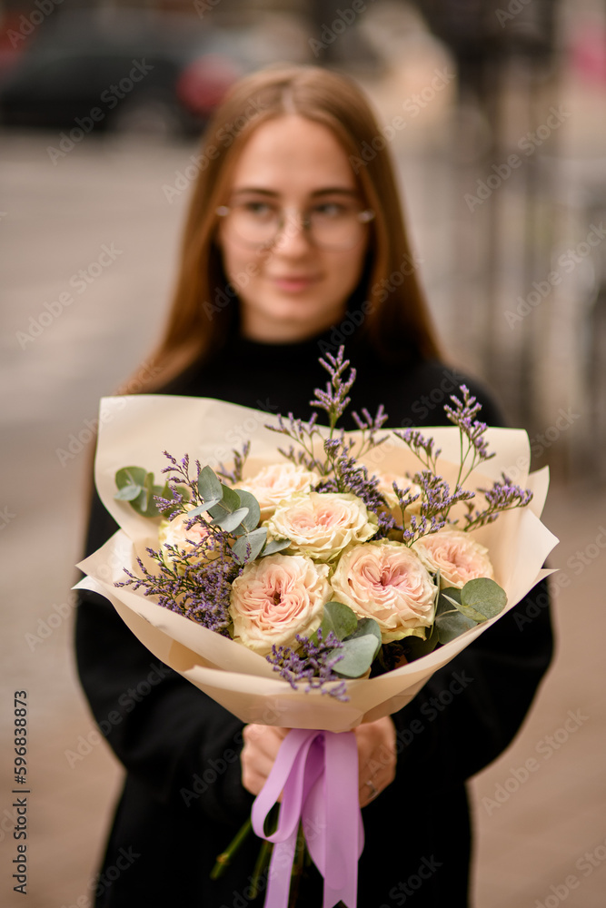 Young woman dressed in black holding in hands big flower bouquet Young woman dressed in black holding in hands big flower bouquet