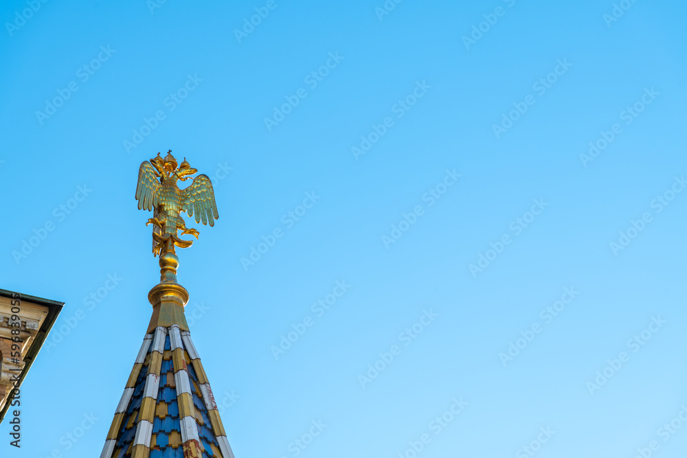 Golden double-headed eagle, coat of arms of Russia, on tower top of Church of the Savior on Spilled Blood in a sunny day in Saint Petersburg city. Clear blue sky. Copy space. National symbols theme. Golden double-headed eagle, coat of arms of Russia, on tower top of Church of the Savior on Spilled Blood in a sunny day in Saint Petersburg city. Clear blue sky. Copy space. National symbols theme.