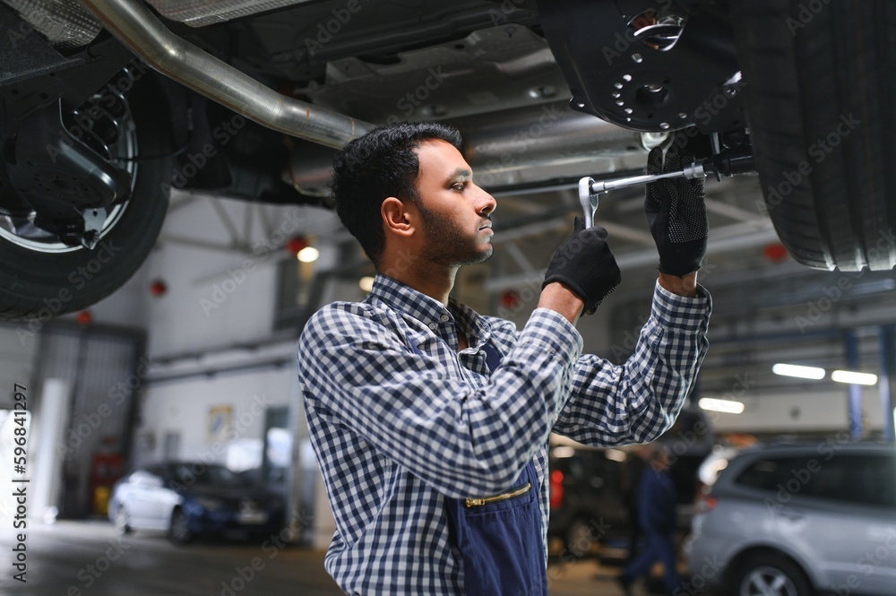 Indian car mechanic standing and working in service station. Car specialists examining the