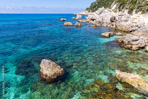 Fototapeta Naklejka Na Ścianę i Meble -  A beautiful landscape of the coast of the island of Corfu in the Ionian Sea of the Mediterranean in Greece. Pure blue clear water washes over the shores of the Greek island.