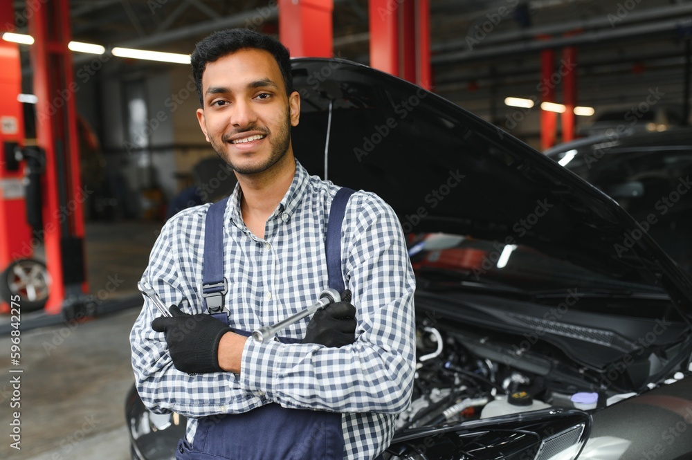 Indian car mechanic standing and working in service station. Car specialists examining the lifted car. Professional repairmen wearing mechanic uniform in blue color. Indian car mechanic standing and working in service station. Car specialists examining the lifted car. Professional repairmen wearing mechanic uniform in blue color.