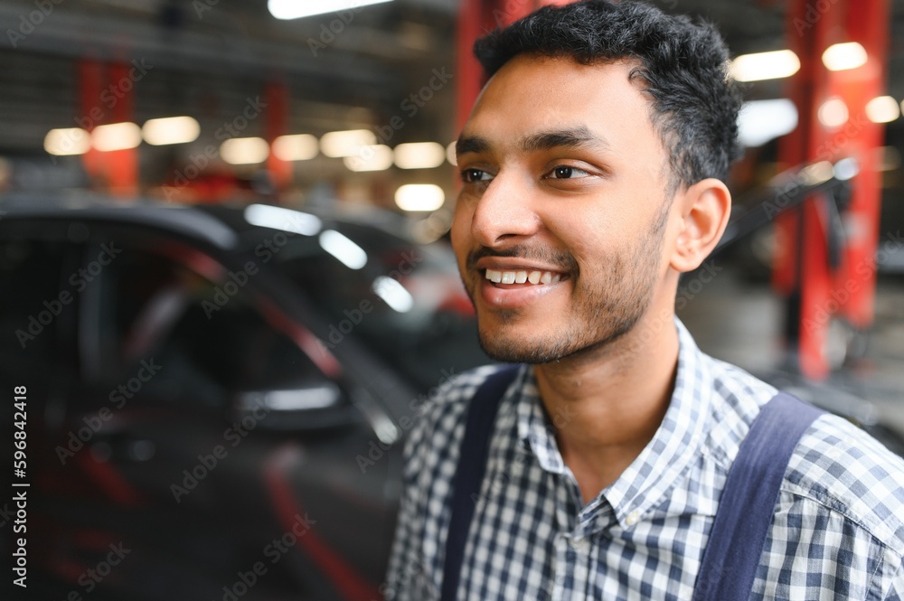 Indian car mechanic standing and working in service station. Car specialists examining the lifted car. Professional repairmen wearing mechanic uniform in blue color. Indian car mechanic standing and working in service station. Car specialists examining the lifted car. Professional repairmen wearing mechanic uniform in blue color.