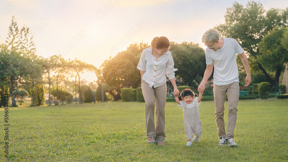 Asian father and mother walking with daughter in park, Parents hold the baby's hands, Happy family in the park evening light. Happy family concept. Asian father and mother walking with daughter in park, Parents hold the baby's hands, Happy family in the park evening light. Happy family concept.