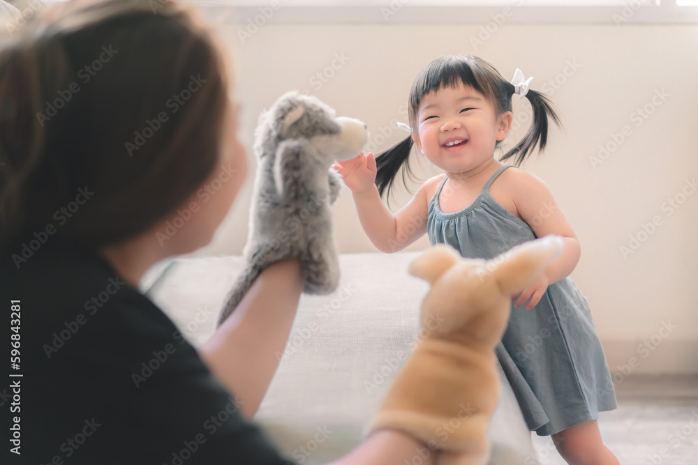 Asian mother and daughter playing animal hand puppet doll toys, sitting on couch, Educational preschool games, Having fun with kid at home concept. Asian mother and daughter playing animal hand puppet doll toys, sitting on couch, Educational preschool games, Having fun with kid at home concept.