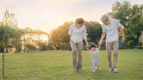 Asian father and mother walking with daughter in park, Parents hold the baby's hands, Happy family in the park evening light. Happy family concept.