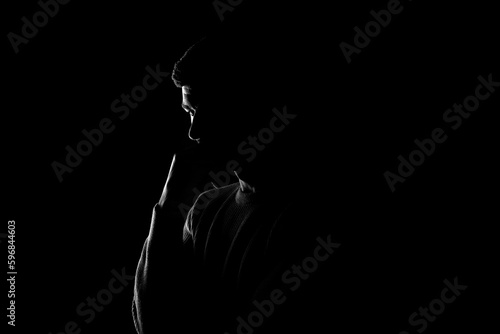 Male silhouette on a black background. A man stands thoughtfully on a black background