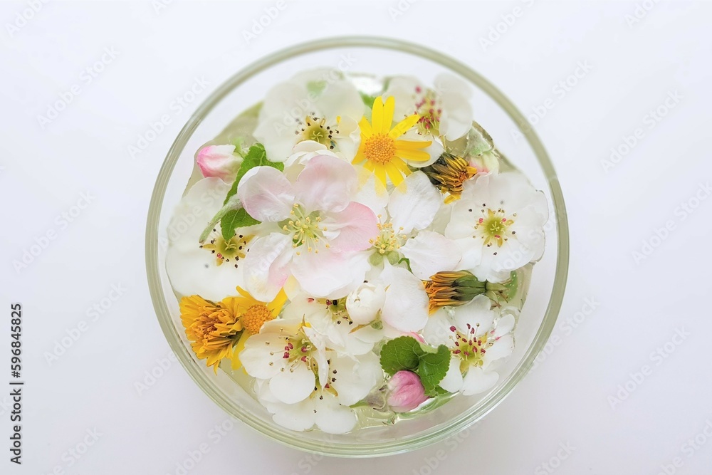 Yellow dandelions and white blooming flowers in a glass bowl with water on a white table Yellow dandelions and white blooming flowers in a glass bowl with water on a white table