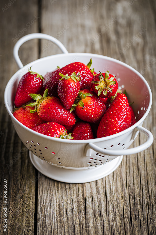 Strawberries in white colander placed on a rustic wooden background. Fresh and tasty seasonal ripe and fruit. Strawberries in white colander placed on a rustic wooden background. Fresh and tasty seasonal ripe and fruit.