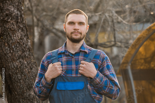 Farmer satisfied european appearance male rural portrait with beard, shirt and overalls man looking at camera outdoors