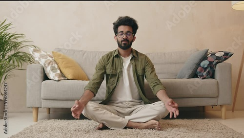 Relaxed indian man doing yoga exercise in living room at home
