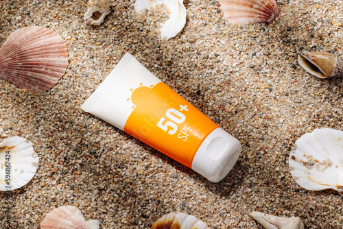 Orange tube of sunscreen on sandy beach top view photo