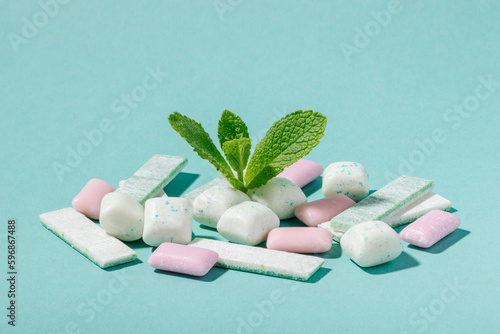 A bunch of mint and fruit chewing gum and fresh mint leaves on a blue background