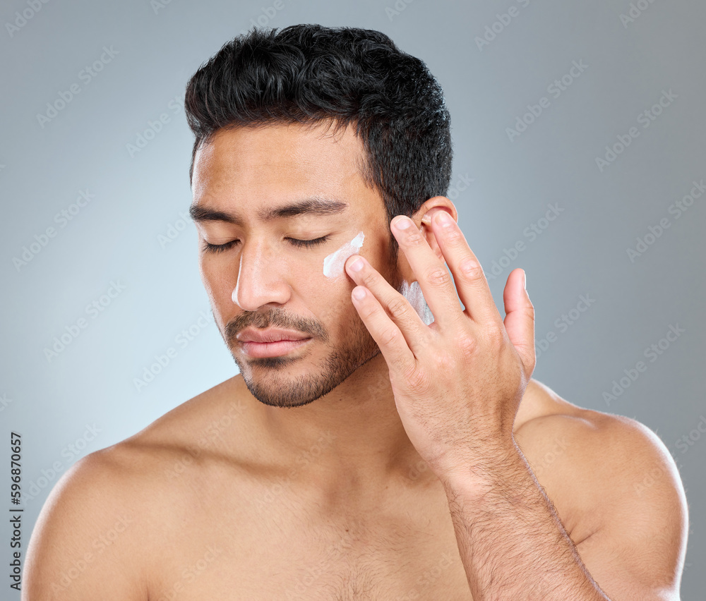 Fototapeta premium Theres nothing wrong with taking care of yourself. Shot of a man applying moisturiser to his face while standing against a grey background.