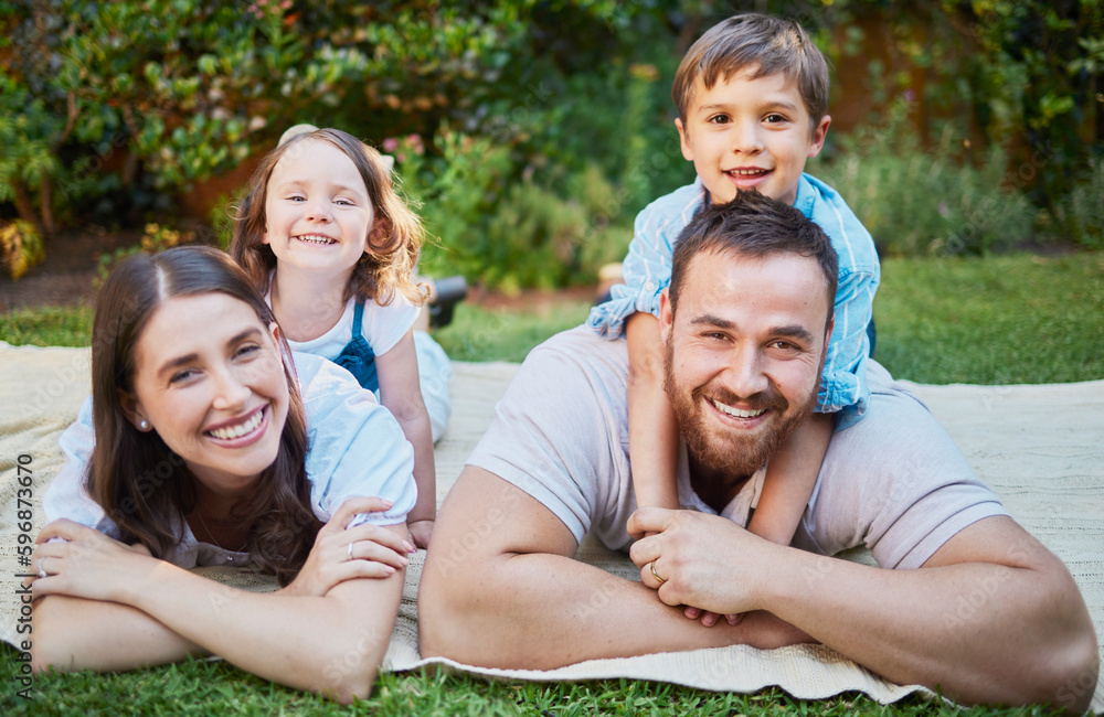 Fototapeta premium Portrait of happy caucasian family lying outside on grass and having a picnic. Cheerful parents and their two children lying on top of them having fun outdoors at park or backyard on a sunny day